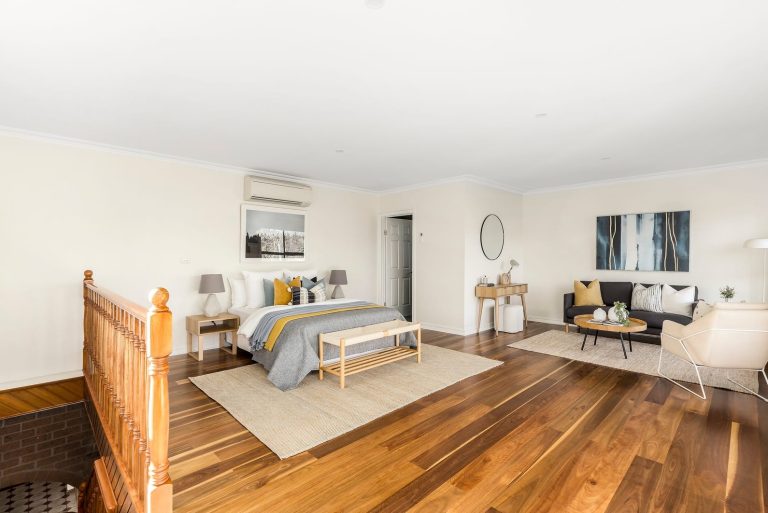 Spacious bedroom styling in Melbourne with warm timber flooring, neutral palette, and integrated lounge zone for added lifestyle appeal