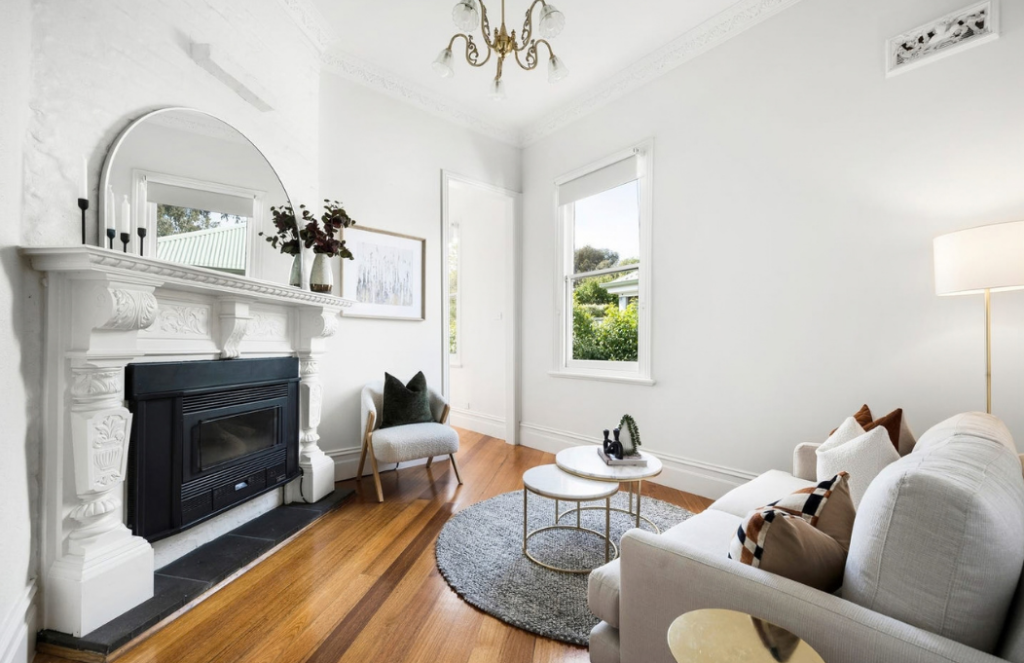 Heritage living room with ornate fireplace, timber floors, neutral sofa and contemporary styling in a house in Brunswick.