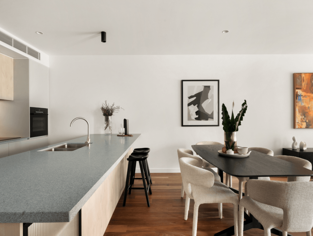 Modern dining area with black dining table, cream upholstered chairs, timber flooring and minimalist artwork in the house in Brunswick.
