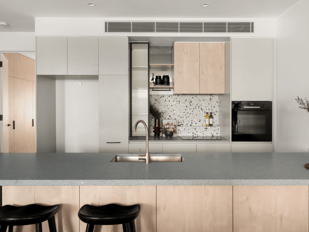 Contemporary kitchen with light timber cabinetry, grey stone island, terrazzo splashback and black bar stools in the house in Brunswick.