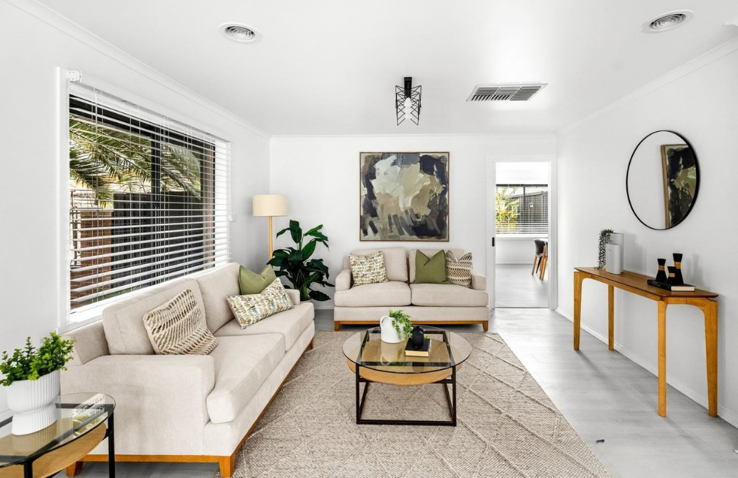 Neutral living room styled with cream sofas, warm timber furniture, black accents and abstract artwork.